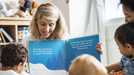 Photo of adult woman reading a story book to young children