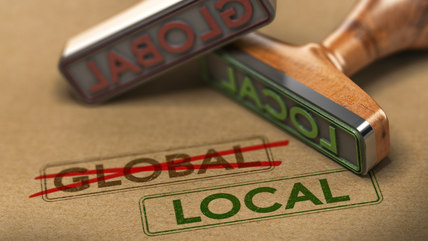 Image of word global and local stamped on brown paper with global crossed out in pen