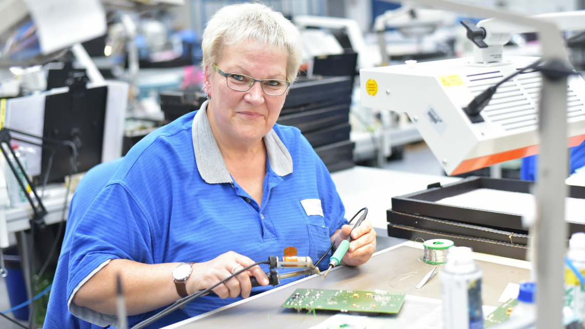 Photo of older woman assembling electronics at factory