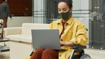 Photo of a young woman in a wheelchair working on a laptop with office building in background