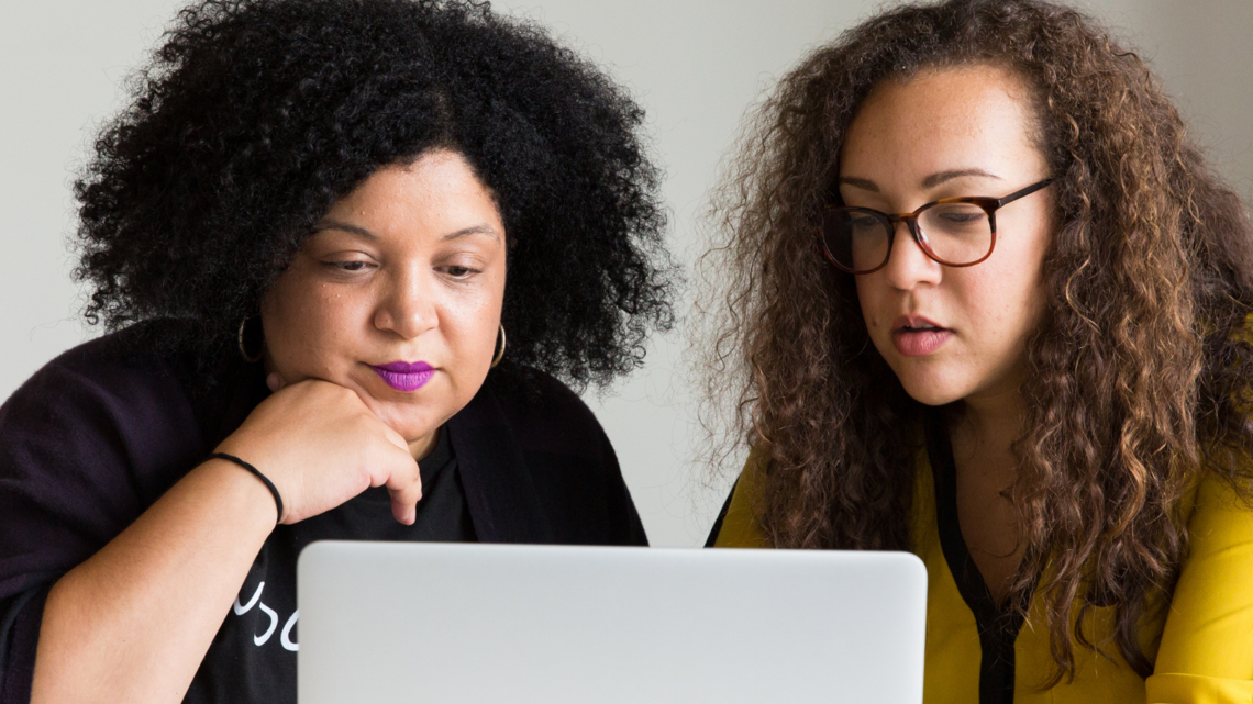 Photo of two young diverse women looking at data on a laptop